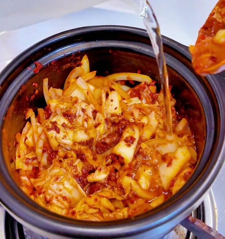 Wasser wird aus einem Behälter in einen schwarzen Topf mit der würzigen Kimchi-Basis gegossen.
