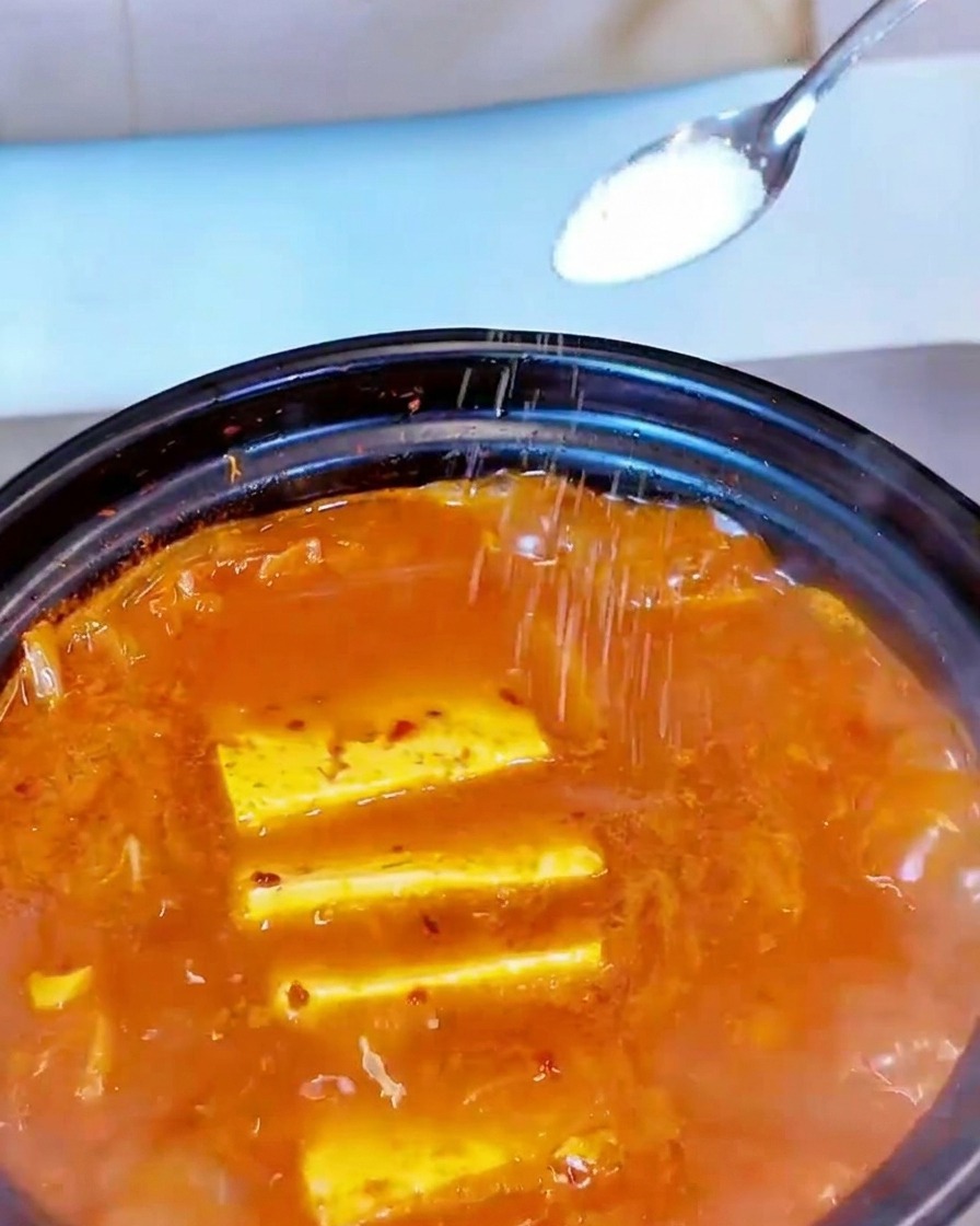 Weißes Salz wird mit einem kleinen Löffel über die köchelnde rote Suppe gestreut.