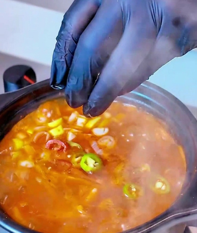 Frisch geschnittene rote und grüne Chiliringe werden als finale Garnitur in den kochenden Topf mit Thunfisch-Kimchi-Suppe gegeben.