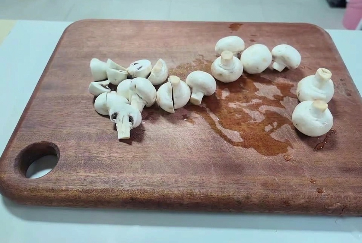 Frische weiße Champignons, die auf einem dunklen Holzbrett in dicke Scheiben geschnitten werden.