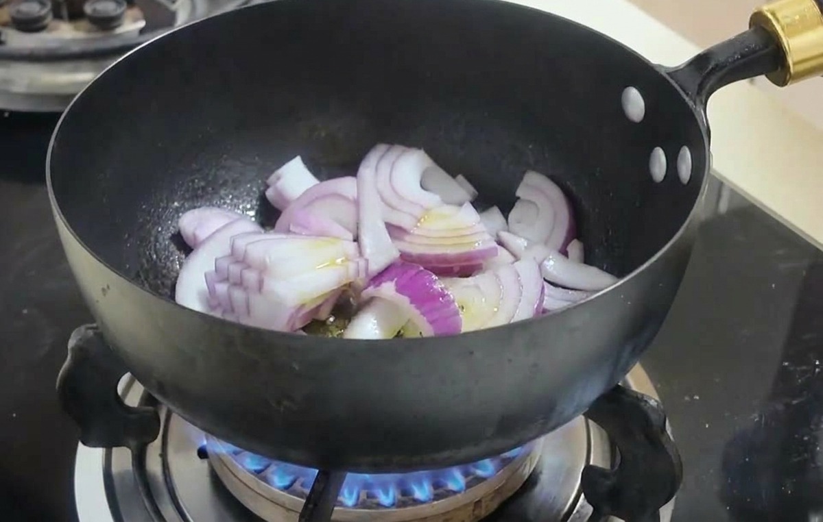 Rote Zwiebelspalten werden in einem schwarzen Wok über einer Gasflamme angebraten.