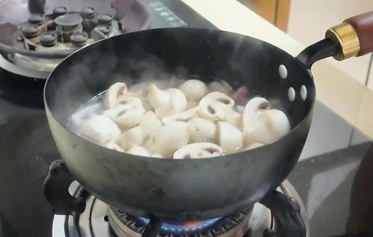 Champignonscheiben und Tofuwürfel köcheln in einer blubbernden Brühe in einer dunklen Pfanne.