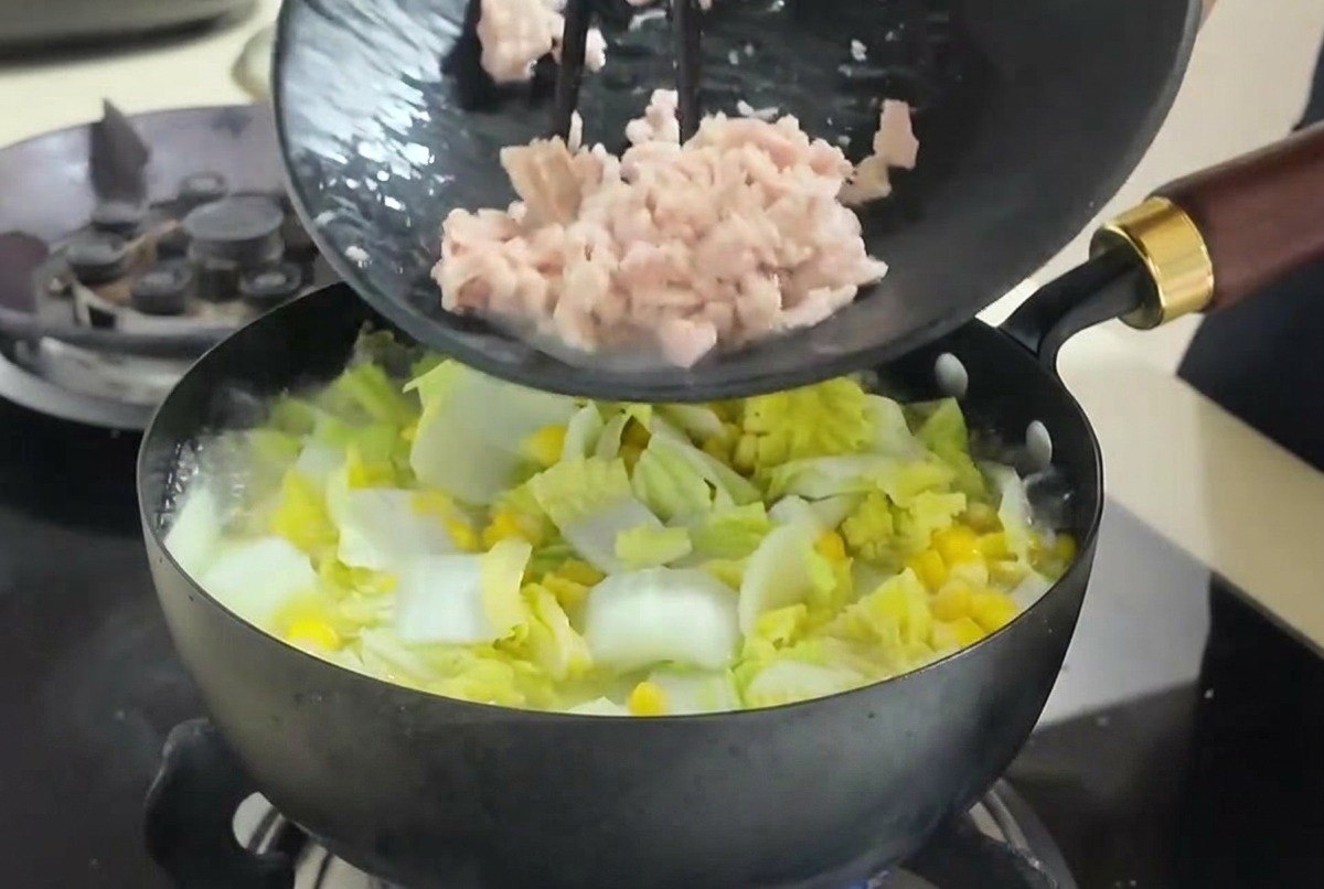 Thunfischstücke werden mit Stäbchen von einem Teller in die kochende Gemüsesuppe geschoben.