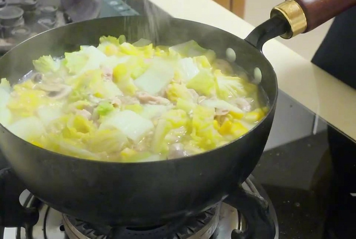 Eine Hand streut Salz in die dampfende Pfanne mit Gemüse, Tofu und Thunfisch.