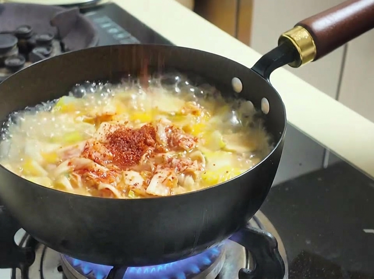 Rotes Chilipulver wird über die kochende Suppe mit Kimchi und Gemüse gestreut.