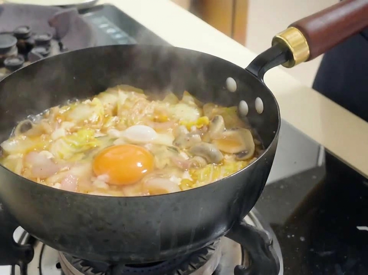 Ein rohes Eigelb liegt in der Mitte der kochenden roten Kimchi-Suppe, umgeben von Kohl und Tofu.