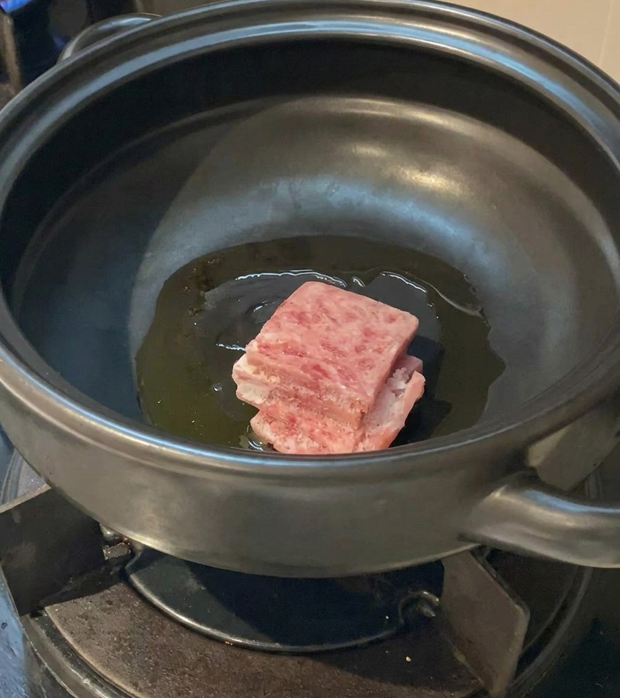 Rohe Scheiben von marmoriertem Schweinebauch werden in das schimmernde Öl im Tontopf gegeben.
