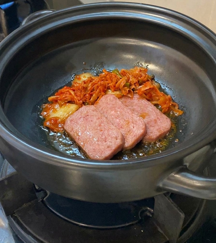 Geschnittenes Kimchi wird zu den angebratenen Fleischscheiben in den Tontopf gegeben.