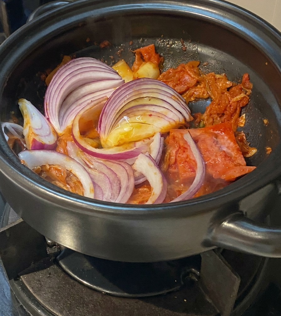 Rote Zwiebelstreifen werden unter das Kimchi und das Fleisch im Topf gerührt.