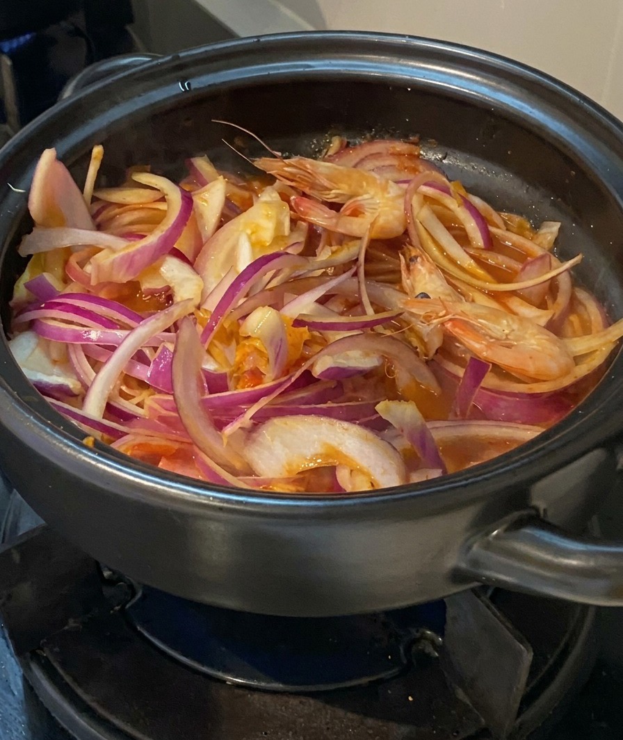 Frische ganze Garnelen werden in den Topf zu den Zwiebeln, dem Kimchi und dem Fleisch gelegt.