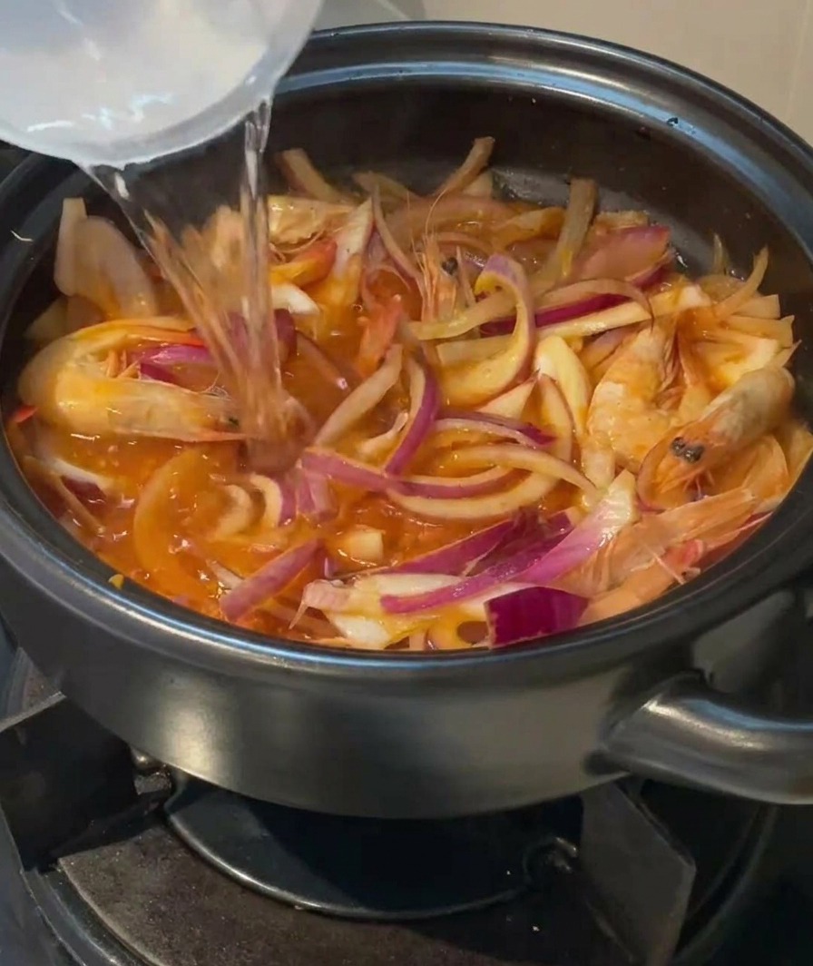 Klares Wasser wird aus einem Gefäß in den Tontopf über die Garnelen und das Kimchi gegossen.