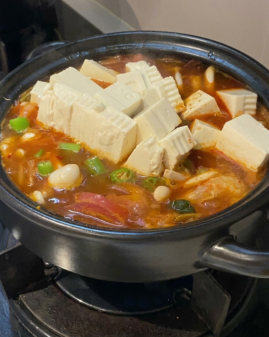 Frische weiße Tofuwürfel und grüne Chilischeiben werden in die rötliche Suppe gegeben.