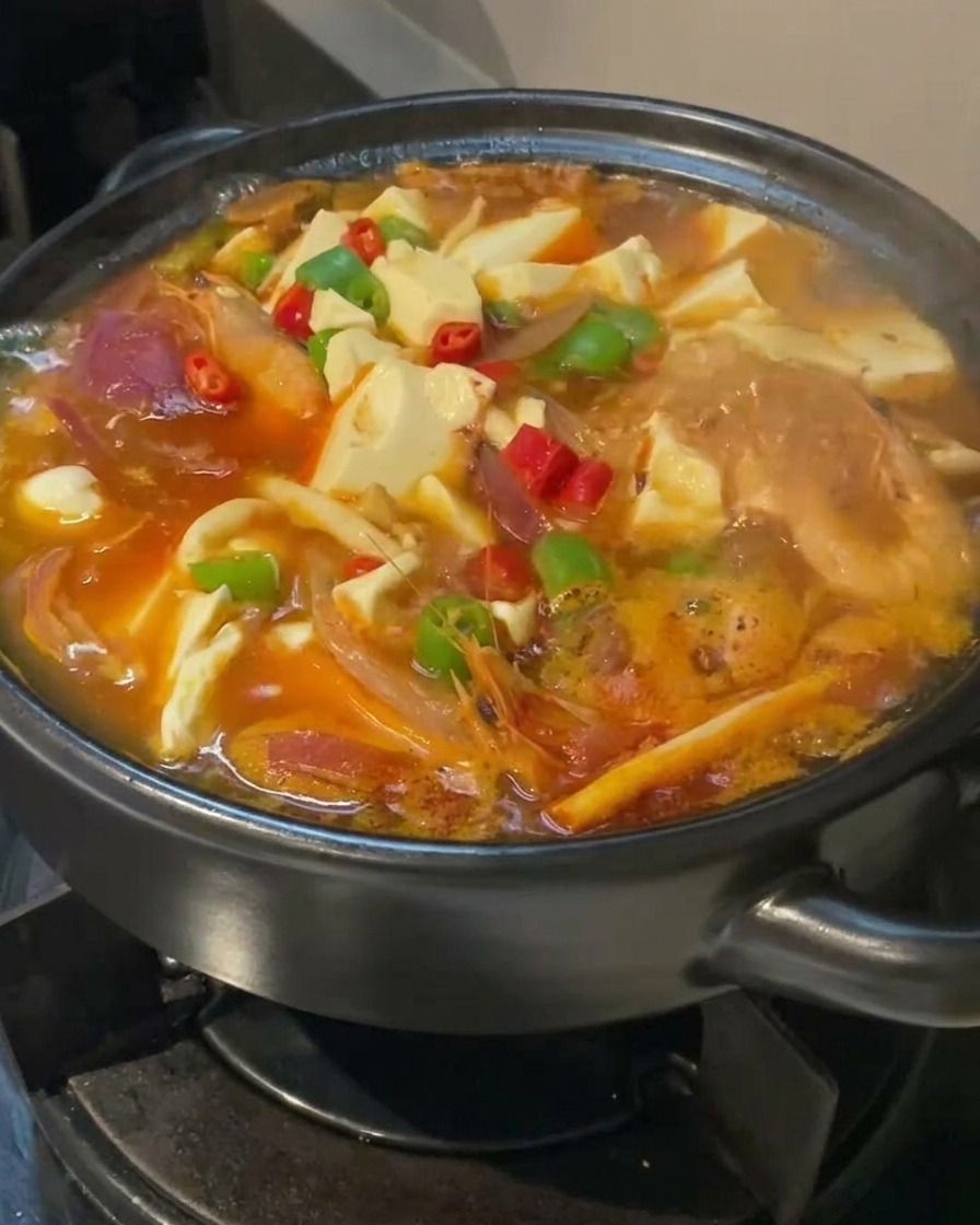 Nahaufnahme der köchelnden Kimchi-Tofusuppe, garniert mit roten und grünen Chilis auf den Tofuwürfeln.
