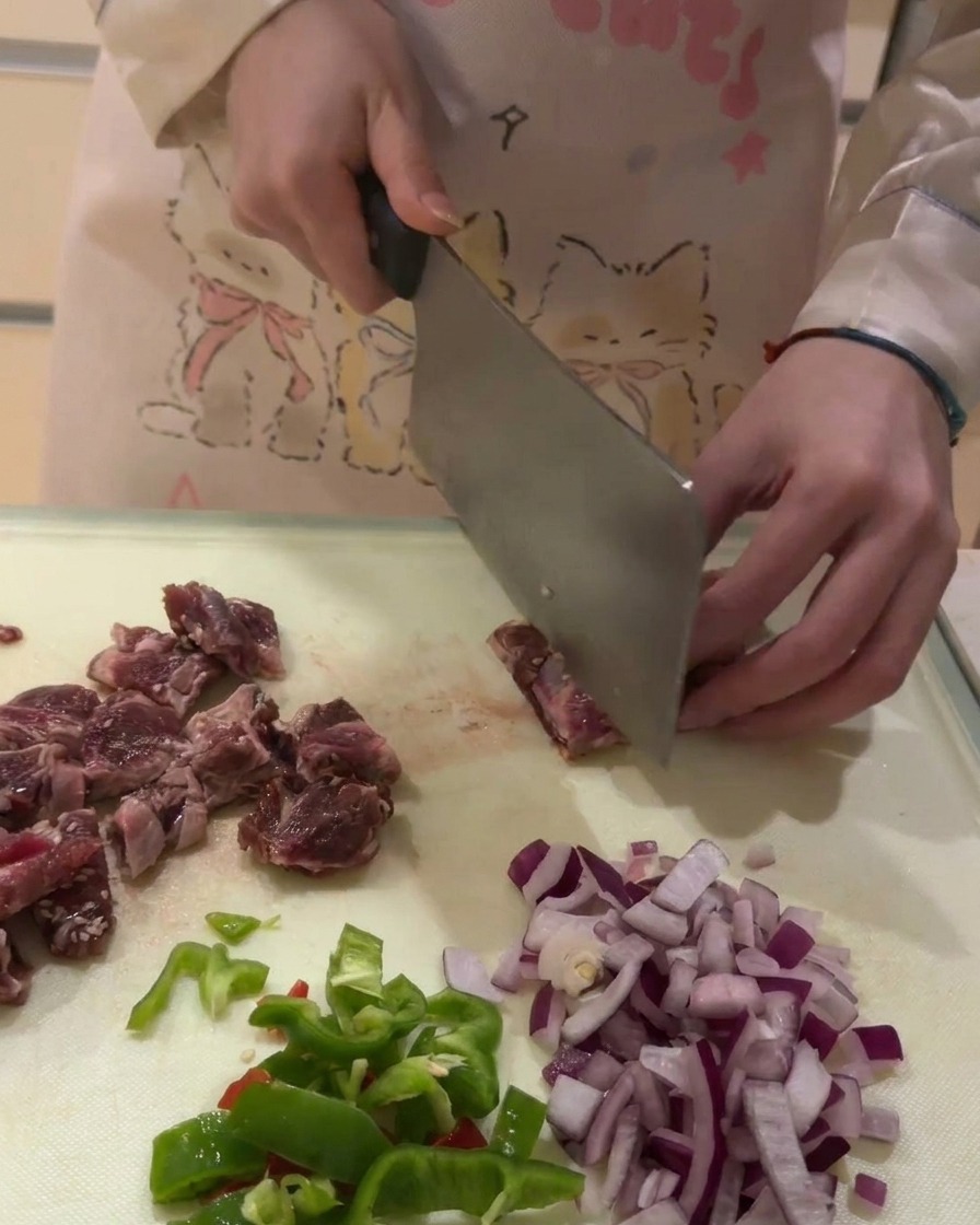 Nahaufnahme von rohem Rinderrippenfleisch, das auf einem weißen Schneidebrett in kleine Würfel geschnitten wird.