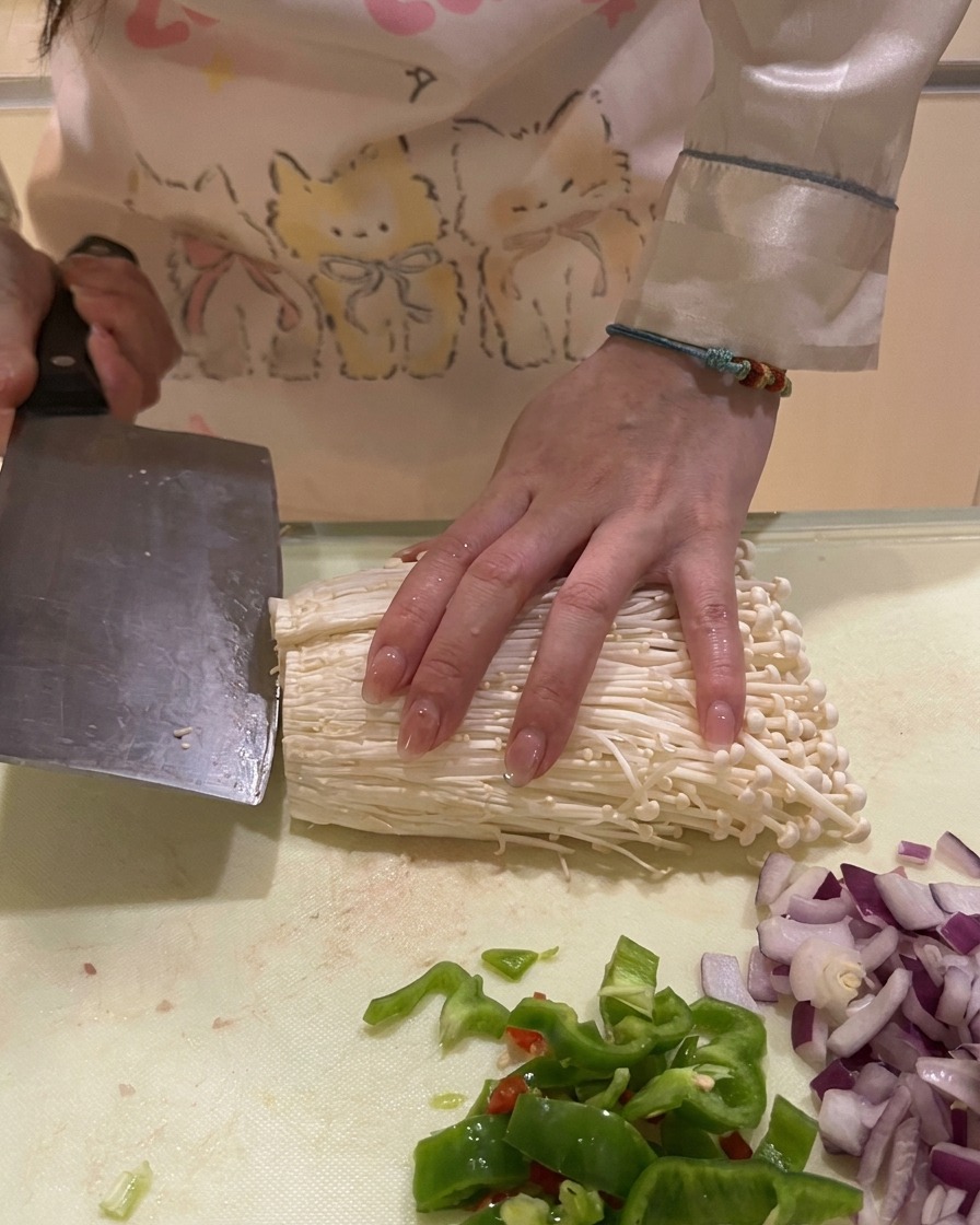 Die unteren Wurzelenden eines Enoki-Pilzbündels werden auf einer Küchenarbeitsplatte abgeschnitten.