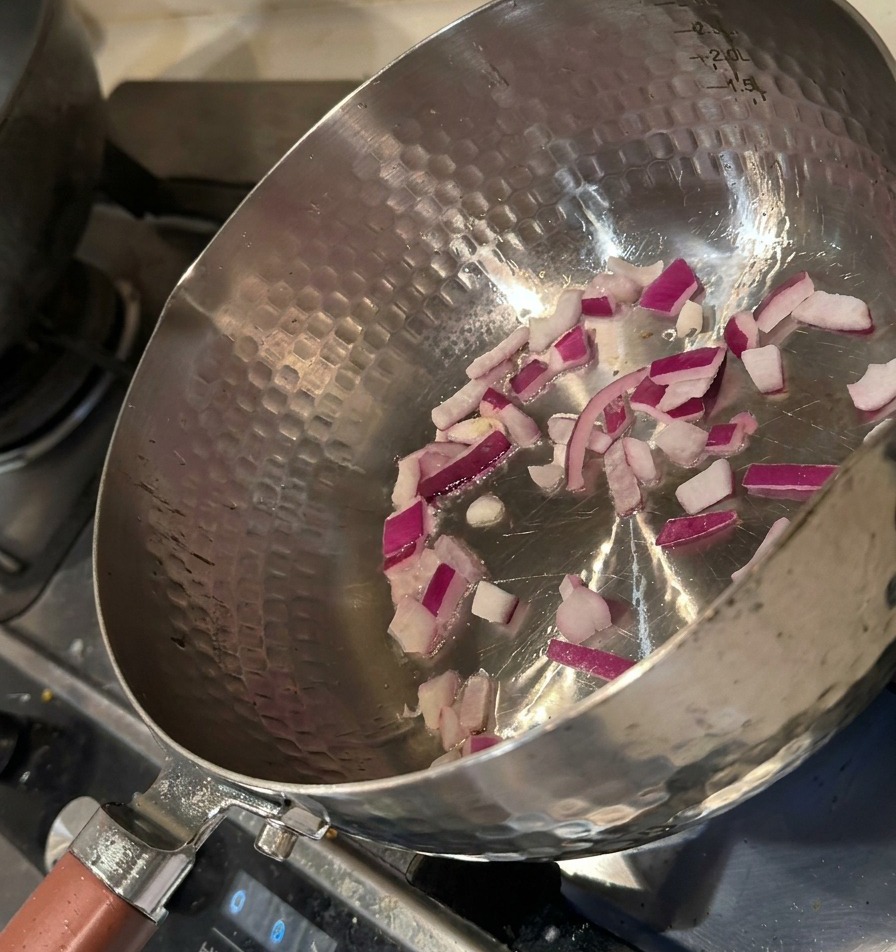 Gehackte rote Zwiebeln werden in einem heißen Metalltopf mit etwas Öl angedünstet.