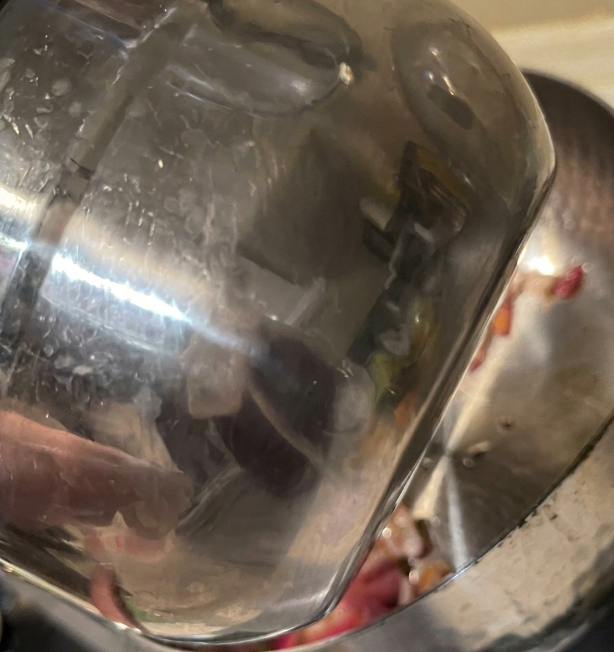 Wasser wird aus einem Edelstahlbecher in einen Topf mit gedünsteten roten Zwiebeln gegossen.