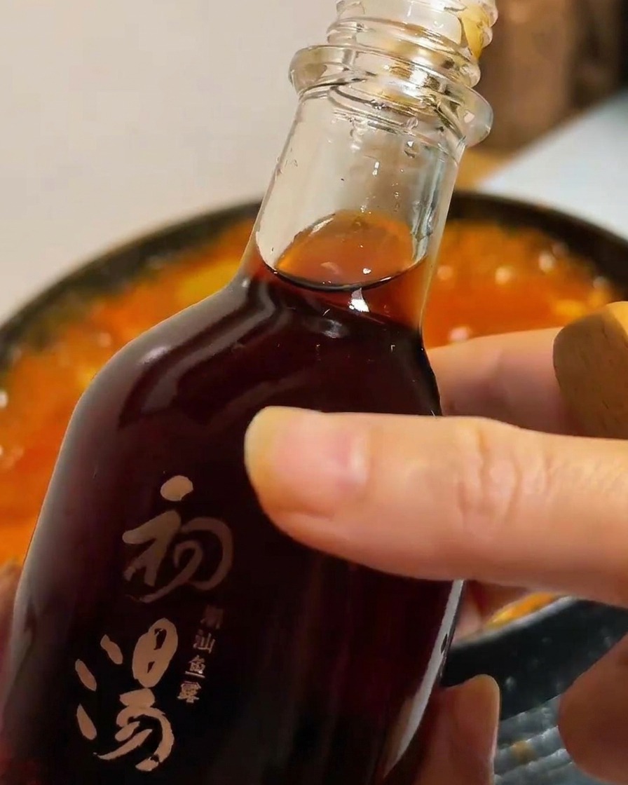 Fischsauce wird aus einer dunklen Glasflasche in den brodelnden Tofu- und Gemüseeintopf gegossen.