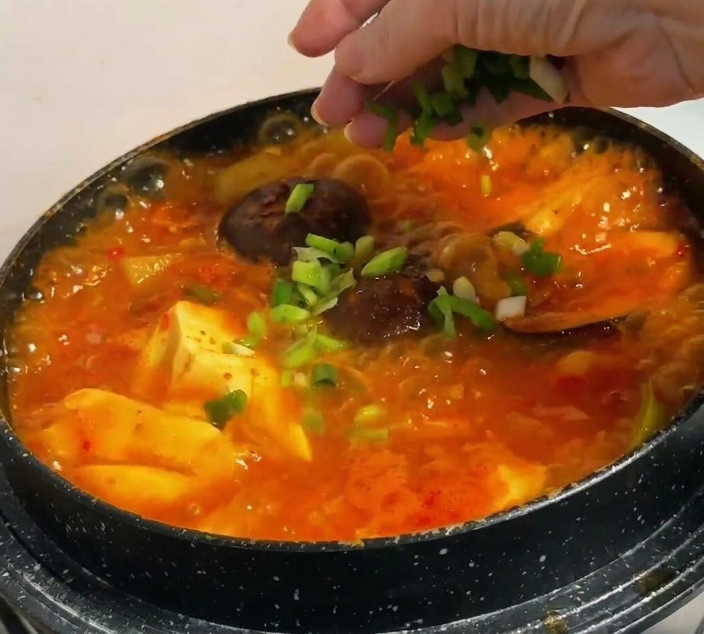 Frische Frühlingszwiebelringe werden über den dampfenden koreanischen Eintopf gestreut.