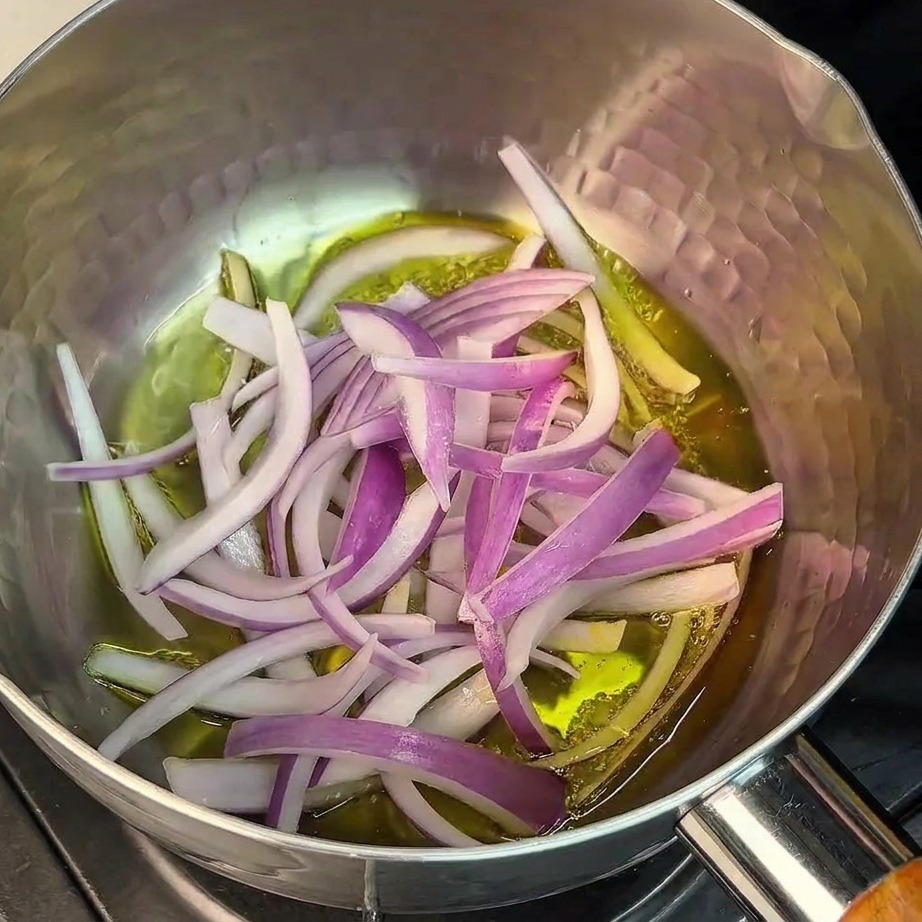 Fein geschnittene rote Zwiebeln werden in einem Edelstahltopf angebraten.