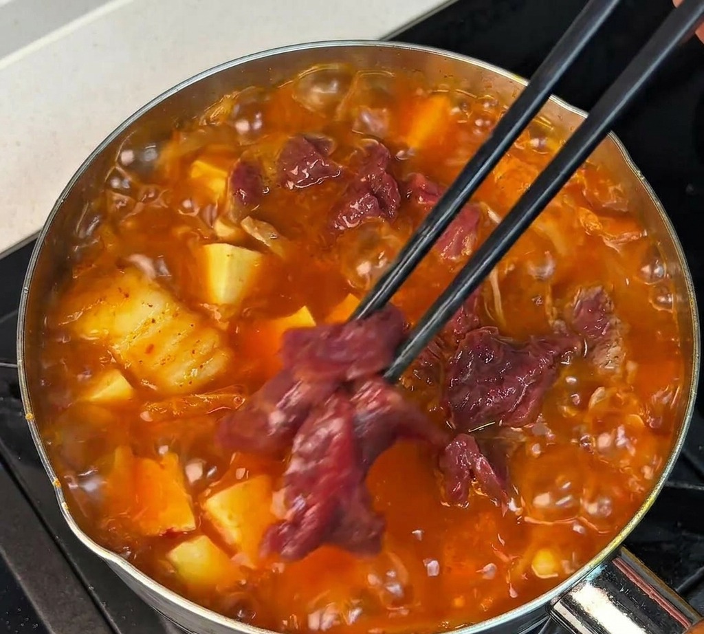 Marinierte Rindfleischstreifen werden mit Stäbchen in die kochende rote Suppe gelegt.