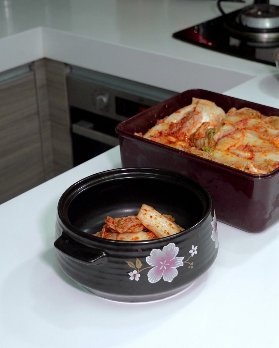 Fermentiertes Kimchi wird mit einer Küchenschere direkt in einem dunklen Keramiktopf zerkleinert.