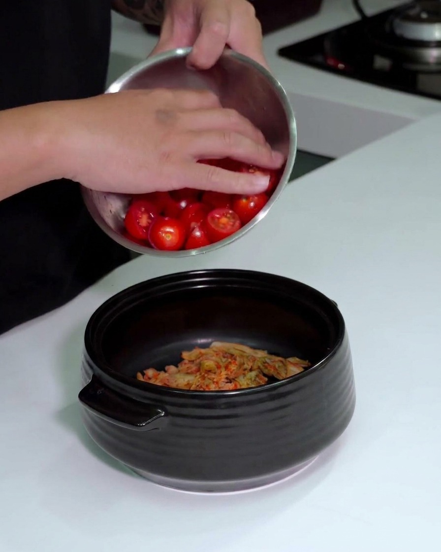Geschnittene Kirschtomaten werden zu dem zerkleinerten Kimchi in den Topf gegeben.