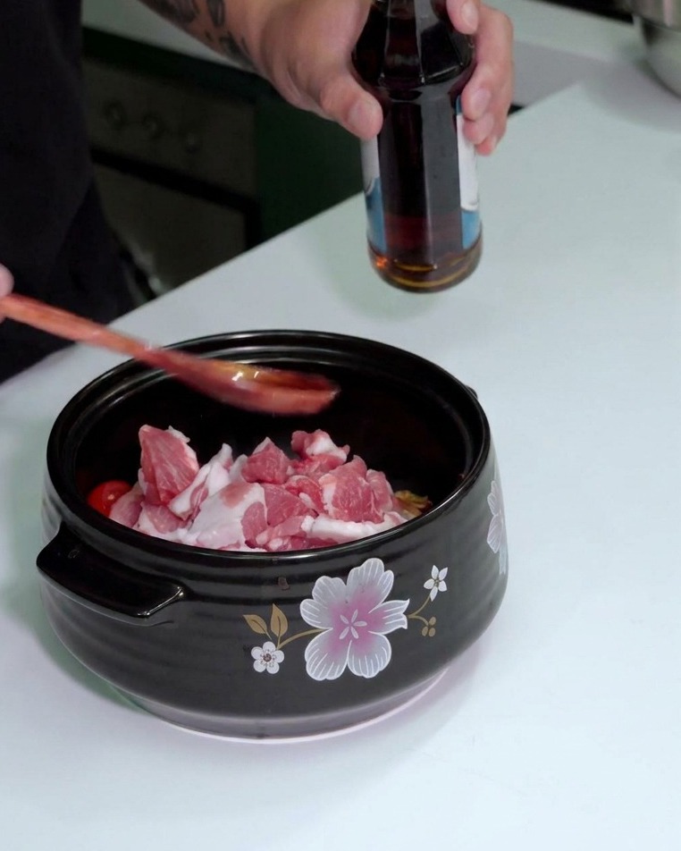 Fischsauce wird aus einer Flasche über einen Holzlöffel in den Topf gegossen.