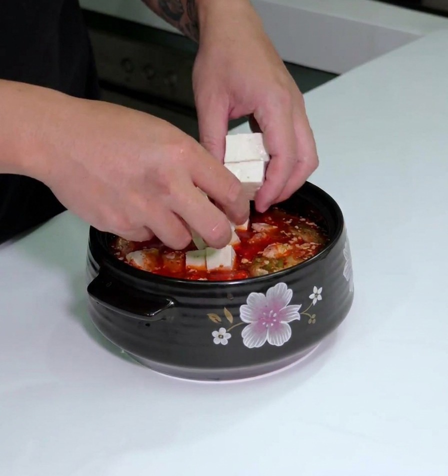 Tofuwürfel werden vorsichtig in die rote Kimchi-Suppe gelegt.