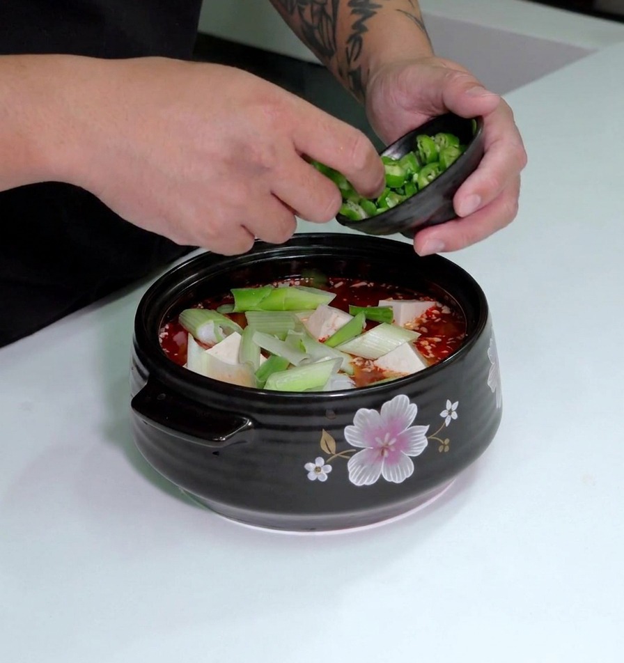 Geschnittene grüne Chilis werden über den Tofu in der Suppe gestreut.