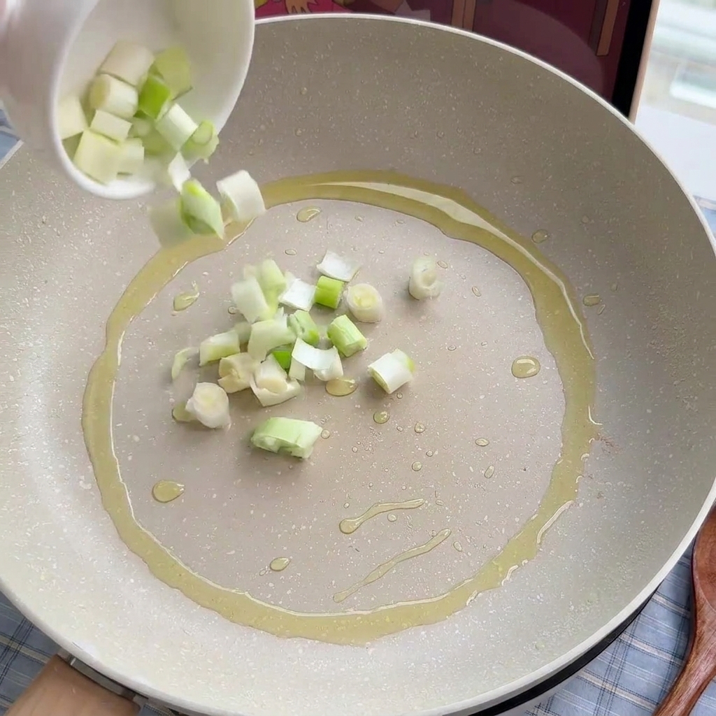 Gehackte Frühlingszwiebeln und Lauchringe werden sanft in einer Pfanne mit Öl angedünstet.