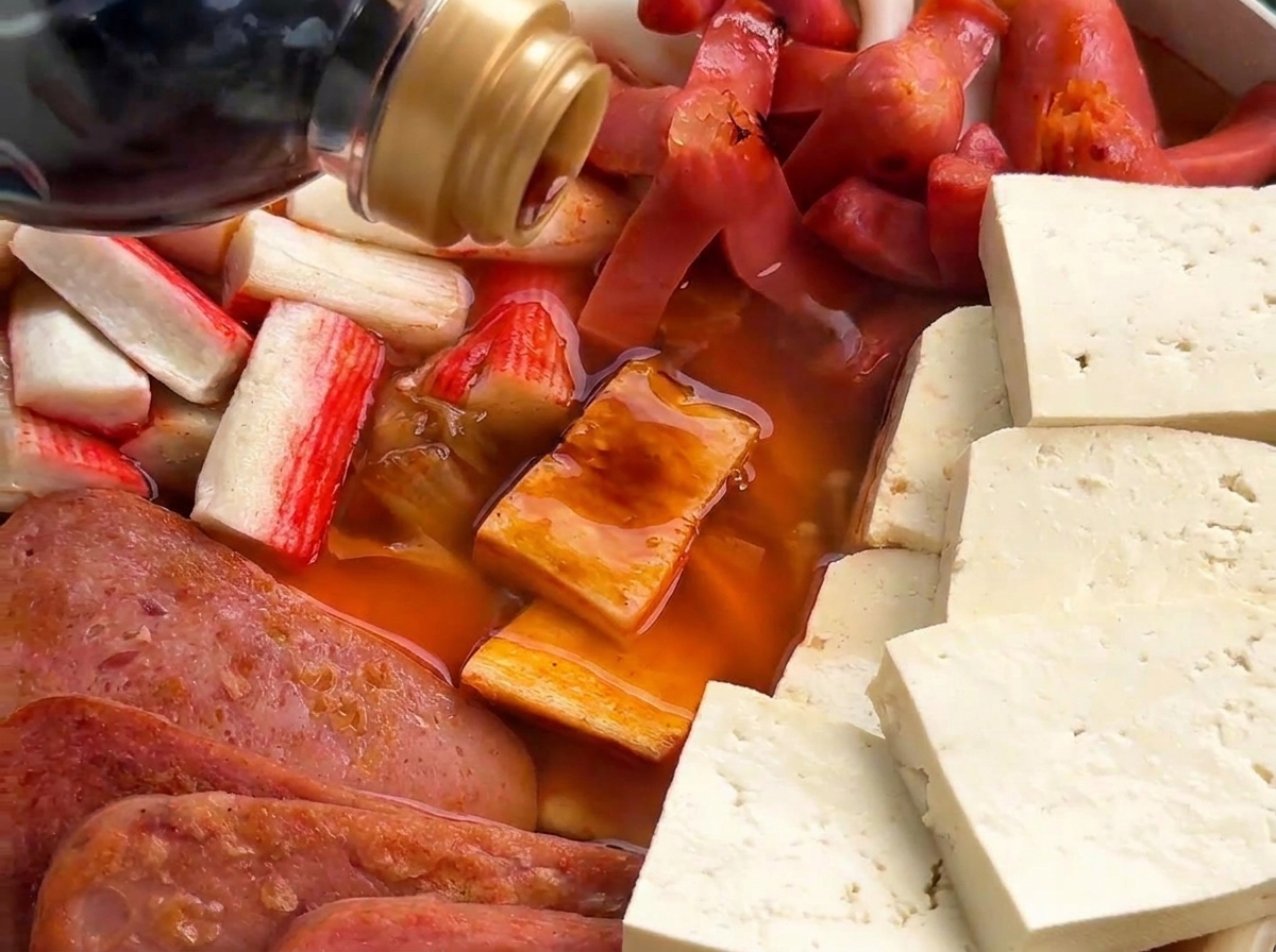 Dunkle Sojasauce wird in den Topf gegossen, in dem Fleisch, Würstchen und Pilze in einer rötlichen Brühe köcheln.