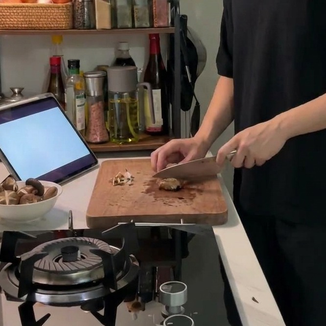 Ein scharfes Messer ritzt ein dekoratives Kreuzmuster in die Oberseite eines frischen Shiitake-Pilzes auf einem Holzbrett.