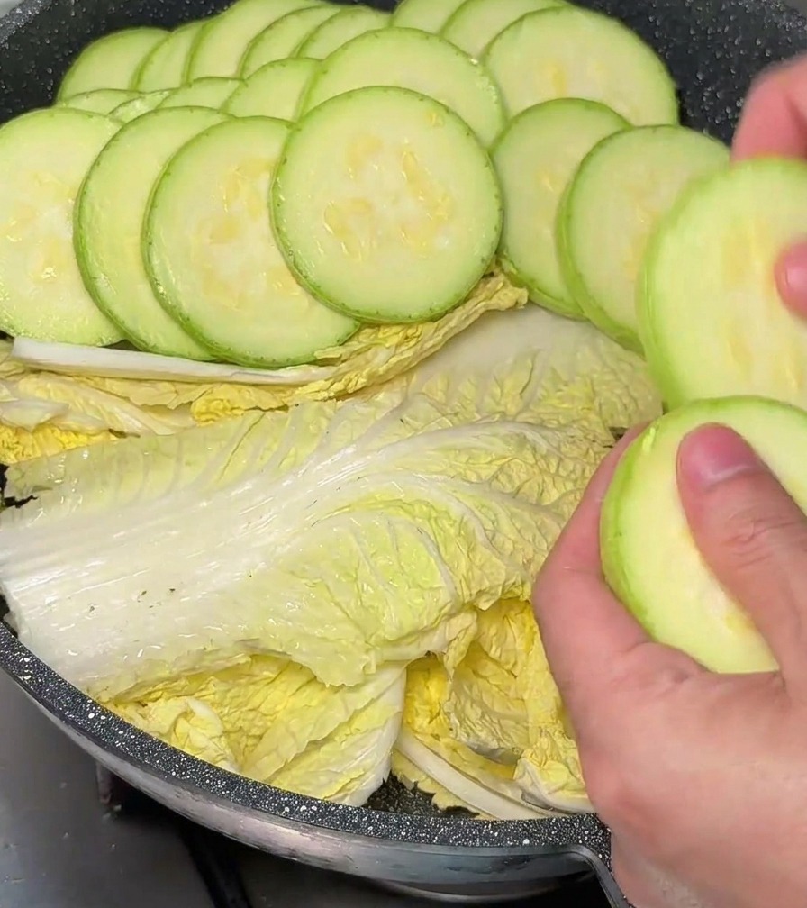 Hände platzieren Zucchini-Scheiben vorsichtig in einem kreisförmigen Muster in einen mit Kohl ausgelegten Topf.