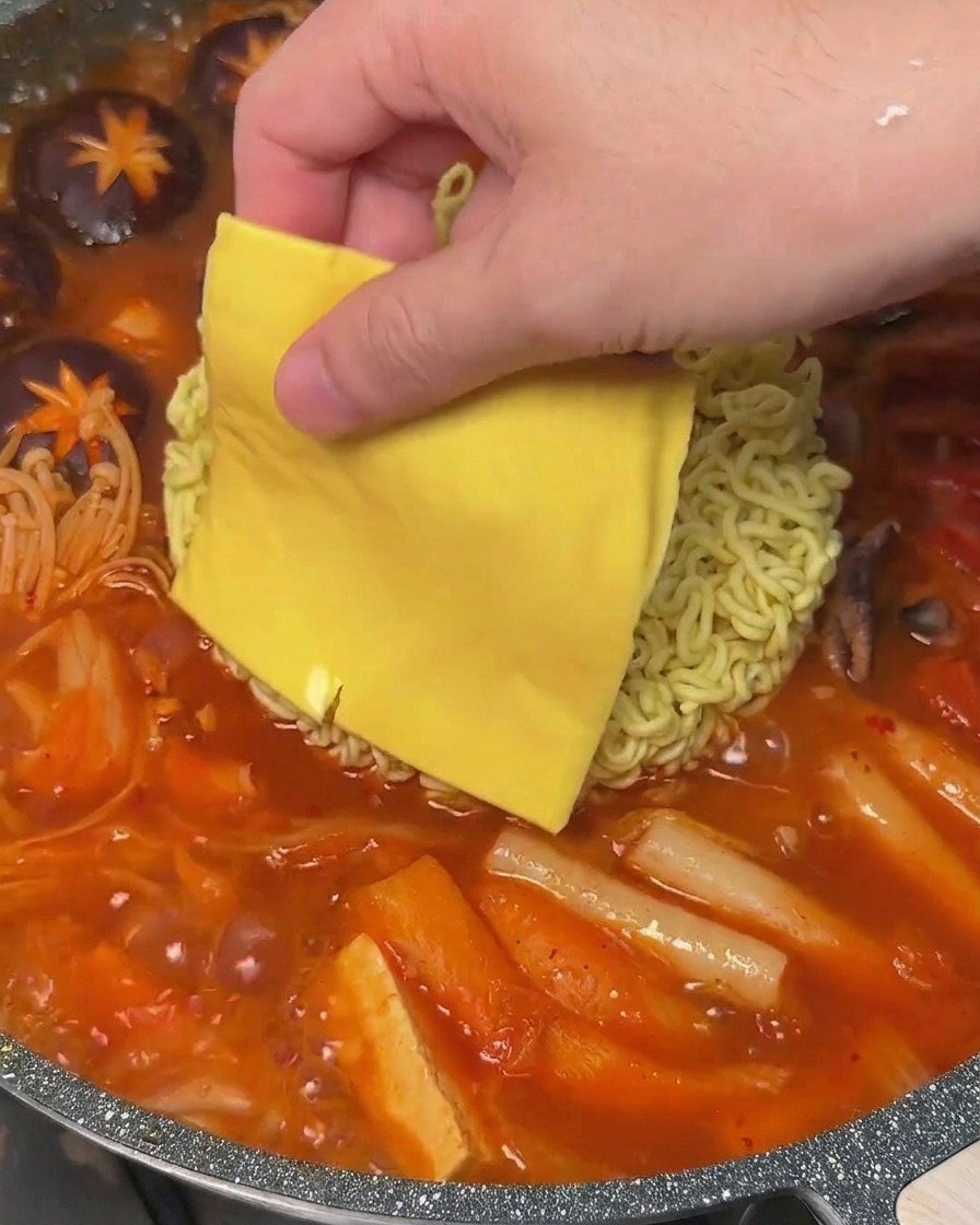 Eine Scheibe gelber Käse wird auf die Instant-Nudeln in einem kochenden Topf Budae Jjigae gelegt.