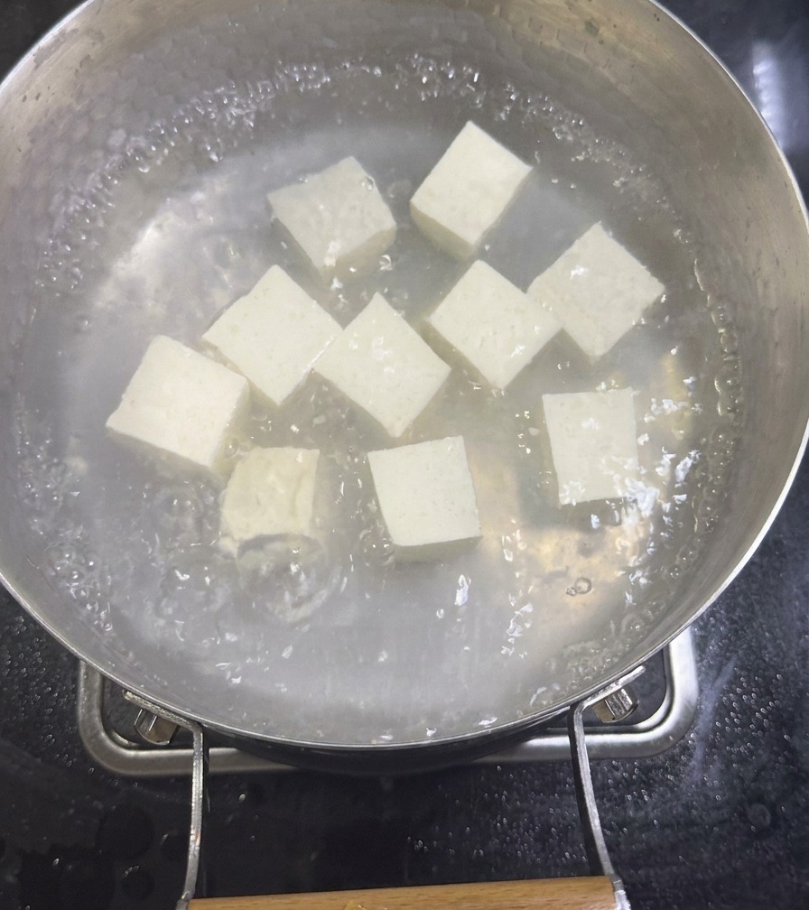 Würfel aus weißem Seidentofu köcheln in einem Topf mit verdünnter Muschelbrühe auf dem Herd.
