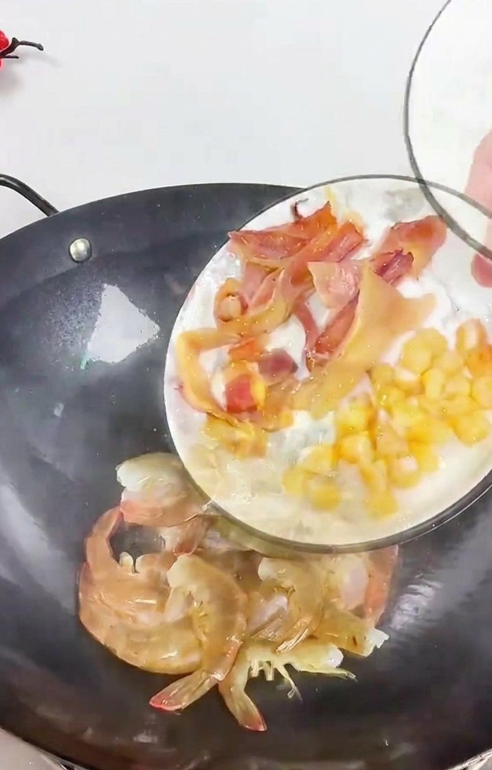 Eine Person gibt geschnittenen Tintenfisch und getrocknete Jakobsmuscheln in einen dunklen Wok zu Garnelen und Ingwerstreifen.