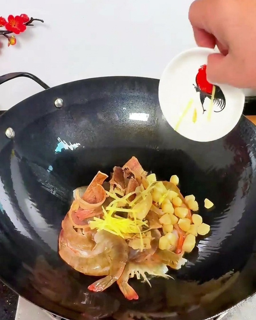 Gelbe Ingwerstreifen werden über eine Mischung aus rohen Garnelen und getrockneten Jakobsmuscheln im Wok gestreut.