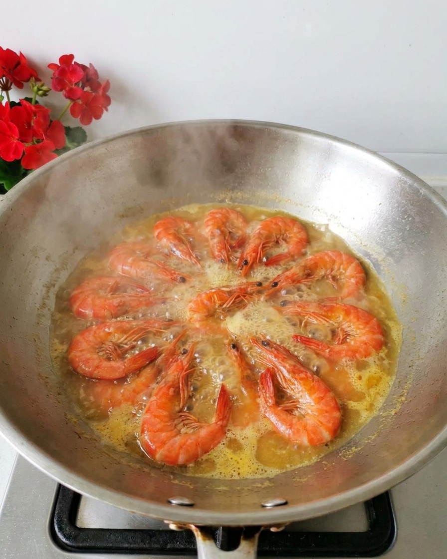 Frische orangefarbene Garnelen kochen in einer hellgelben Brühe in einem Edelstahl-Wok, Dampf steigt auf.