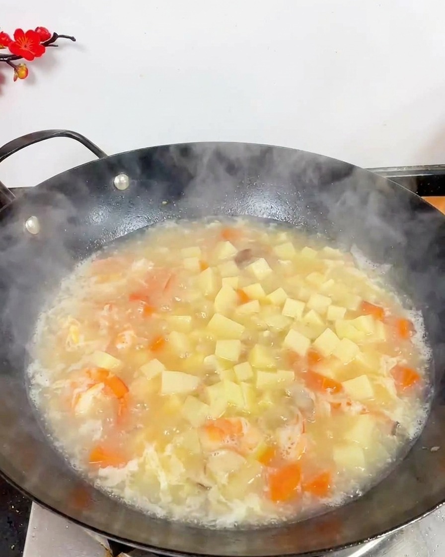 Draufsicht auf einen Wok mit kochender weißer Suppe, Tofuwürfeln, Garnelen und kleinen braunen Pilzen.