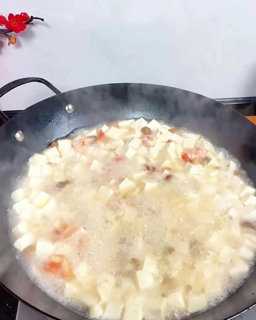 Eine Schöpfkelle aus Edelstahl gießt dunklen Essig in die sprudelnde weiße Suppe mit Tofu und Meeresfrüchten.
