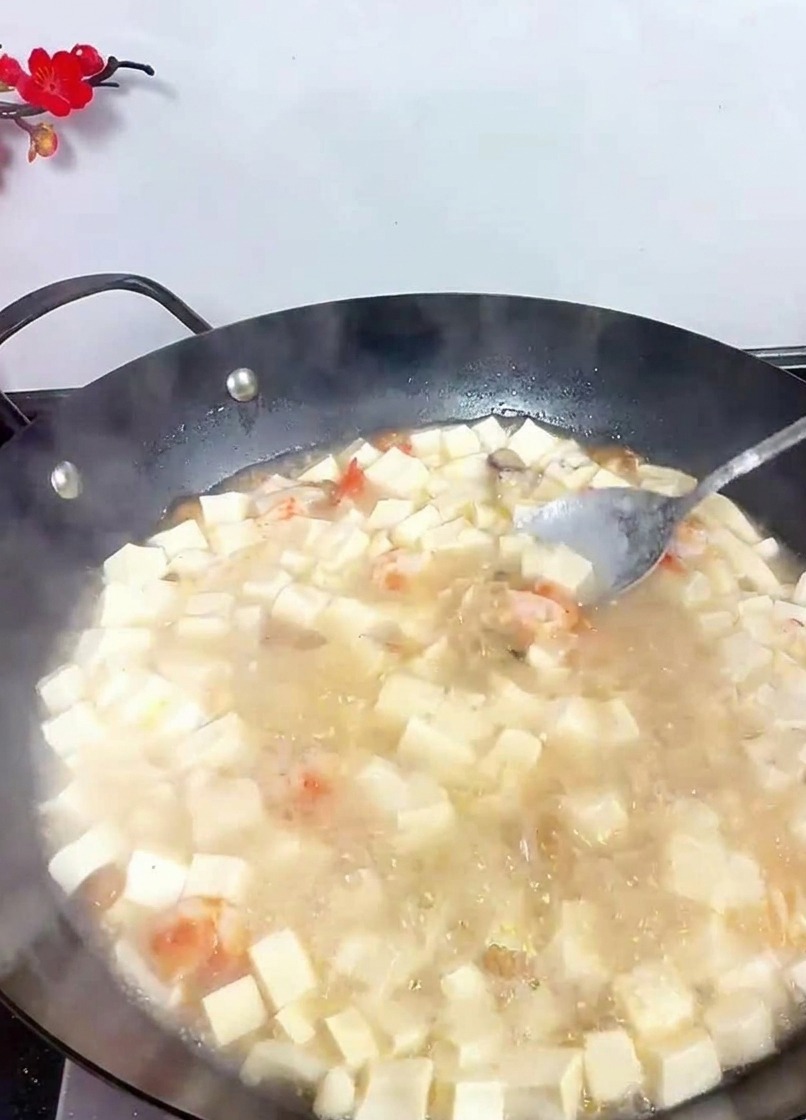 Ein Löffel rührt in einem sprudelnden Wok mit weißer Tofusuppe, um Gewürze zu vermengen.