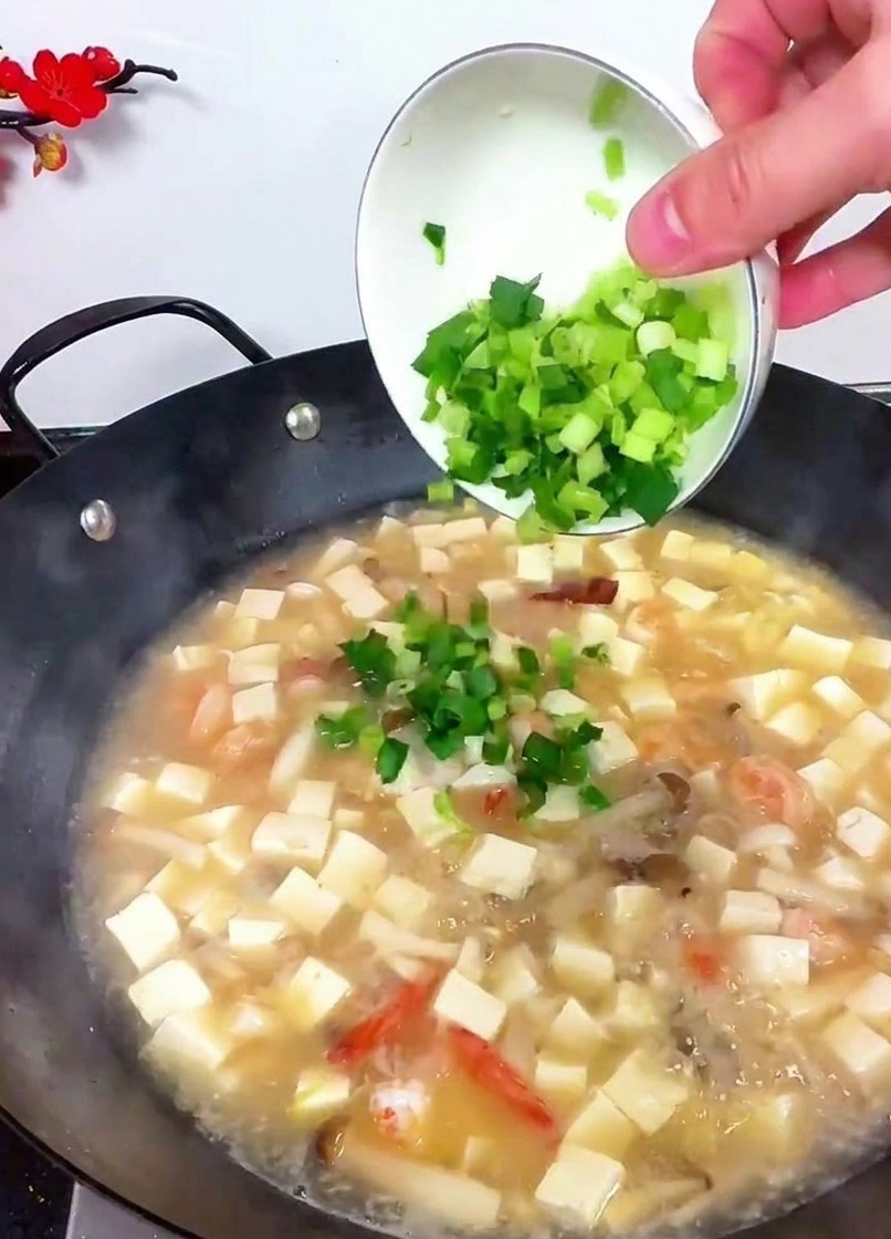 Eine Hand kippt eine kleine weiße Schüssel mit hellgrünem gehacktem Sellerie und Knoblauchsprossen in den Wok.