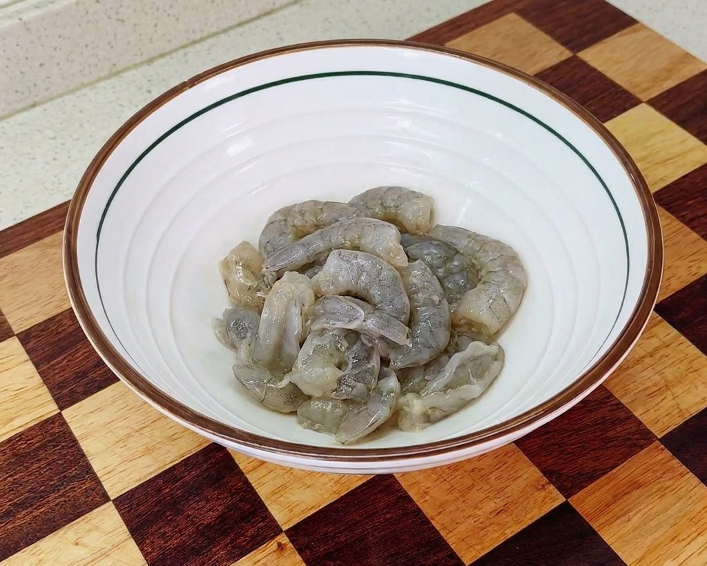 Eine weiße Schüssel mit gesäubertem Garnelenfleisch, das mit Salz, Stärke und Öl mariniert wurde.
