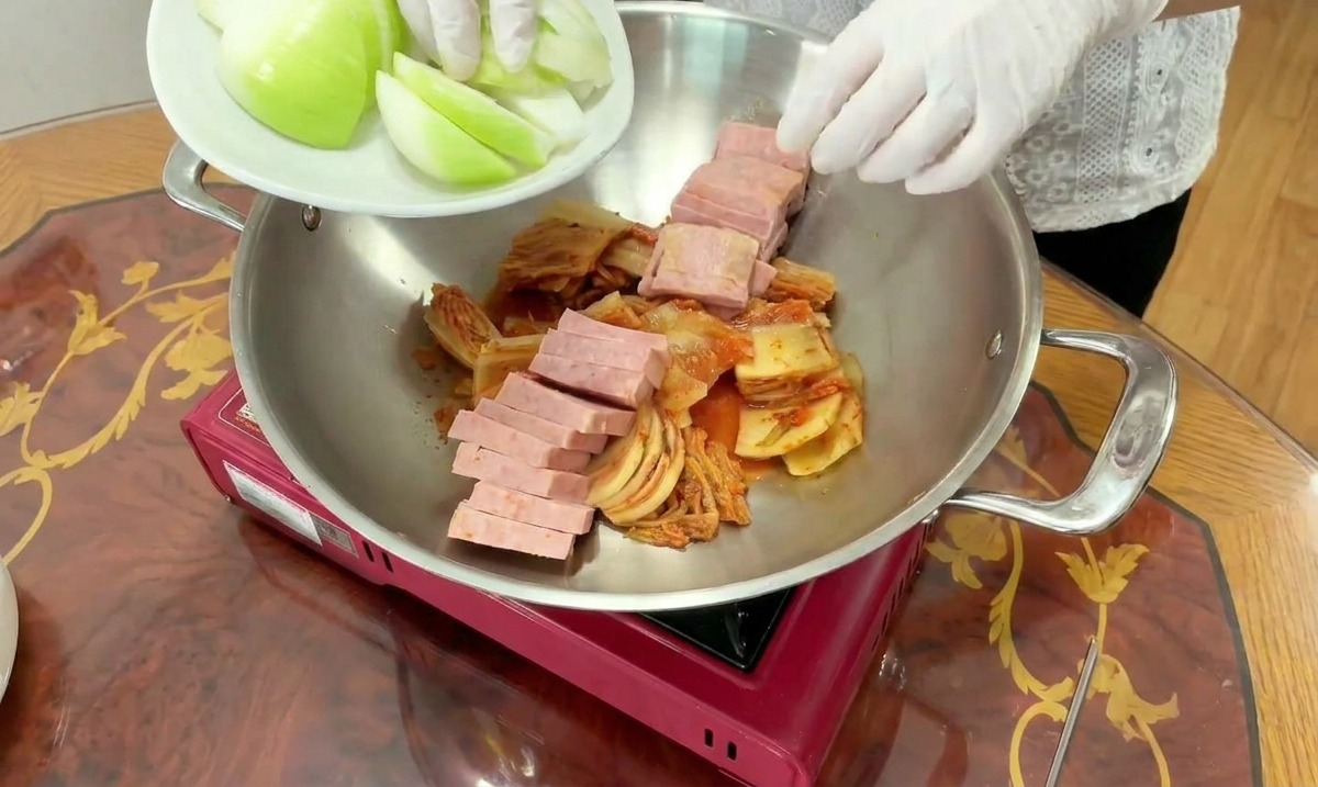 Frische weiße Zwiebelspalten werden zu dem Kimchi und dem Fleisch in den Topf gegeben.