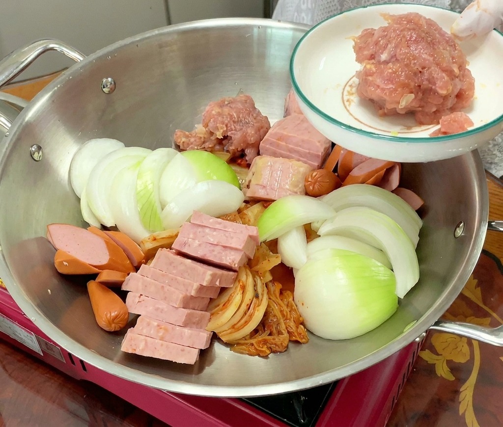 Ein Häufchen gewürztes Schweinehackfleisch wird in den Topf mit Kimchi, Spam und Zwiebeln gegeben.
