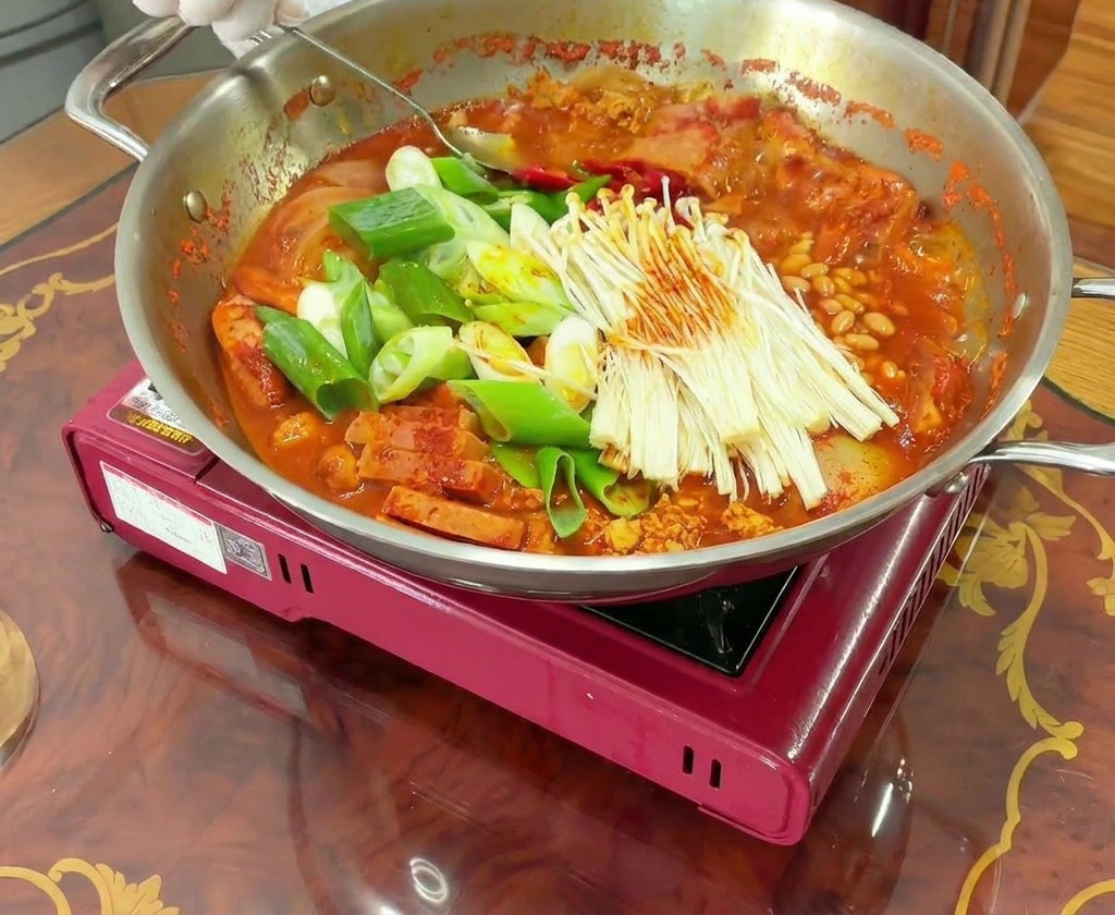 Ein kochender Topf Budae Jjigae wird umgerührt, um die Würzpaste mit der Brühe zu vermengen.