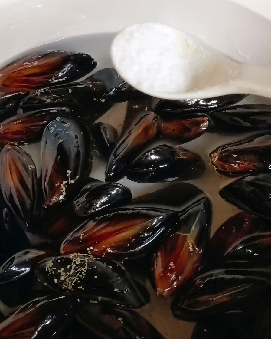 Ein Löffel Salz wird zu schwarzen Miesmuscheln in einen Topf mit Wasser gegeben.
