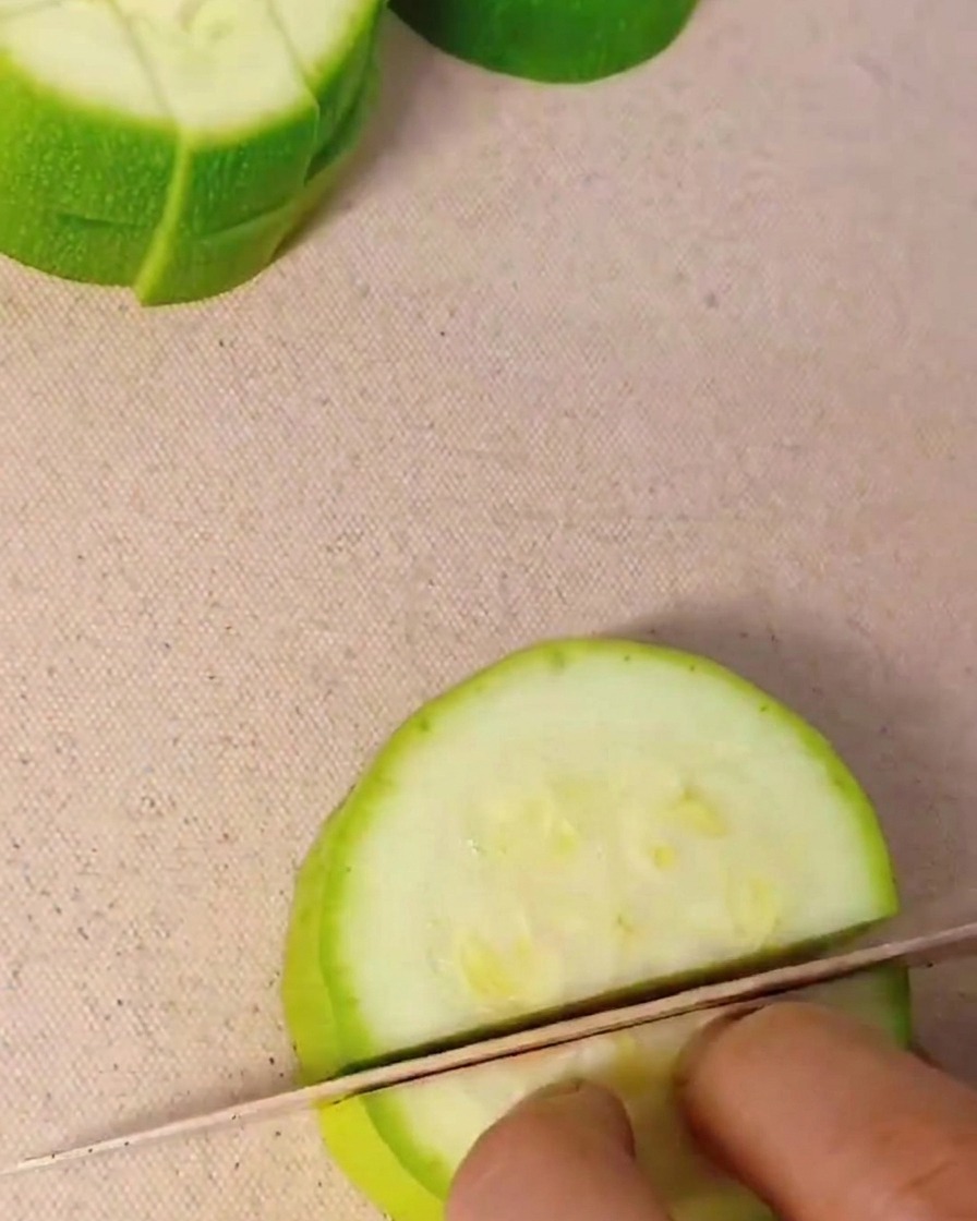 Nahaufnahme einer Hand, die eine frische grüne Zucchini mit einem Küchenmesser in kleine Würfel schneidet.