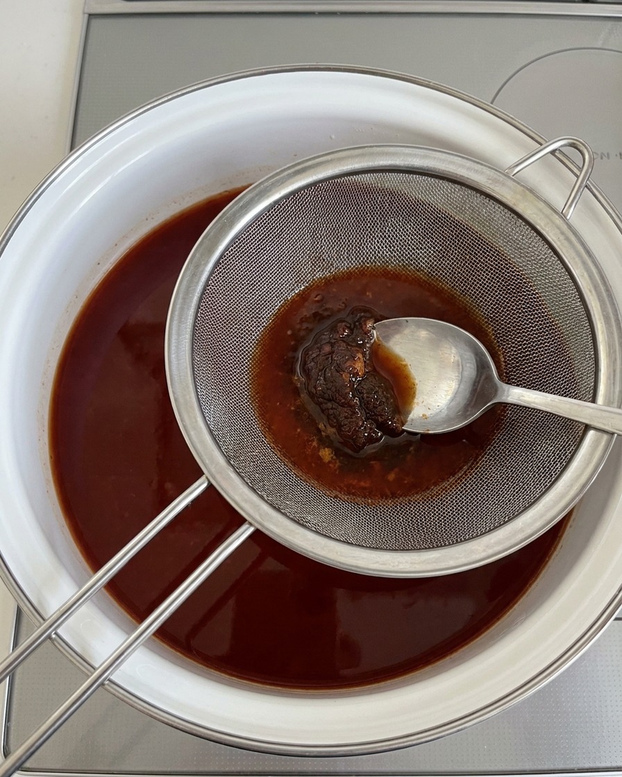 Ein Löffel drückt dicke Sojabohnenpaste durch ein Metallsieb in die kochende Brühe.